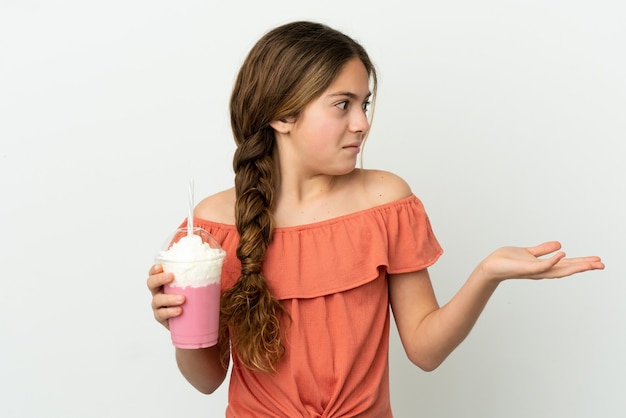 Little caucasian girl with strawberry milkshake isolated on white background with surprise expression while looking side