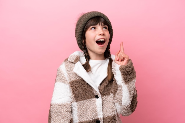 Little caucasian girl with winter jacket isolated on pink background thinking an idea pointing the finger up