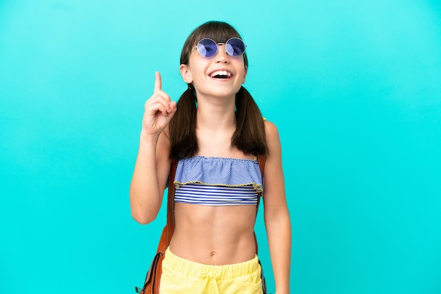 Little caucasian kid going to the beach isolated on blue background pointing up and surprised