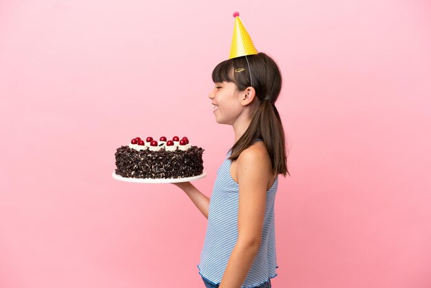 横の位置で笑ってピンクの背景で隔離の誕生日ケーキを保持している小さな白人の子供