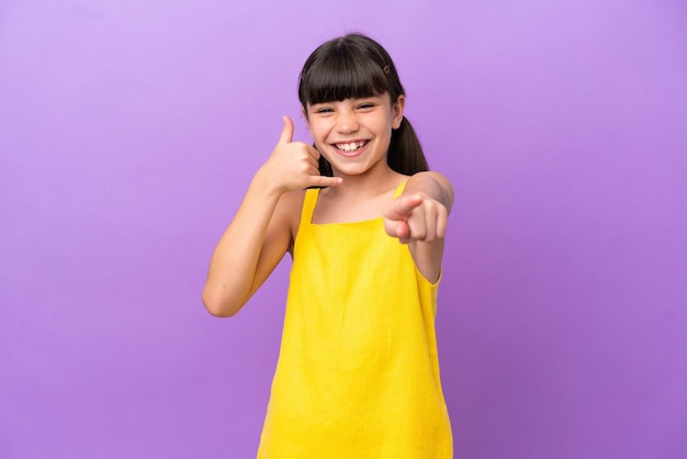 Little caucasian kid isolated on purple background making phone gesture and pointing front