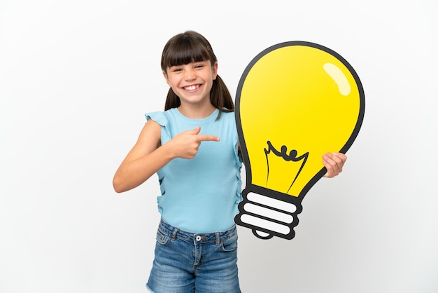 Little caucasian kid isolated on white background holding a bulb icon and pointing it