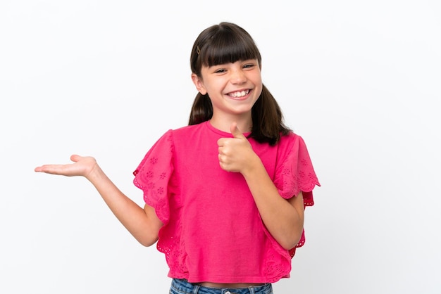 Little caucasian kid isolated on white background holding copyspace imaginary on the palm to insert an ad and with thumbs up