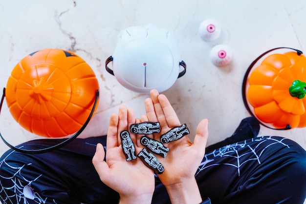 Маленький кавказский ребенок играет с хеллоуинским трюком или угощением конфетным скелетом шоколадом