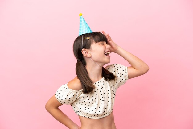 たくさん笑ってピンクの背景に分離された誕生日の帽子を持つ小さな白人の子供