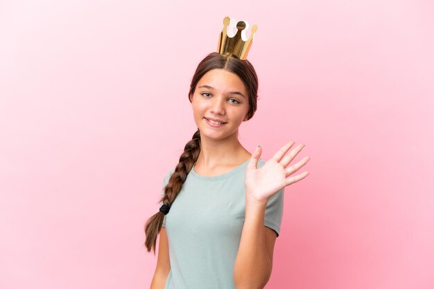 Little caucasian princess girl isolated on pink background saluting with hand with happy expression