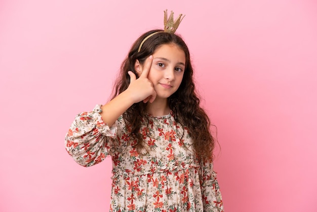 Little caucasian princess with crown isolated on pink background thinking an idea