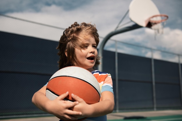 Foto piccolo bambino sportivo caucasico che gioca a basket tenendo la palla con lo stile di vita dei bambini attivi faccia felice po