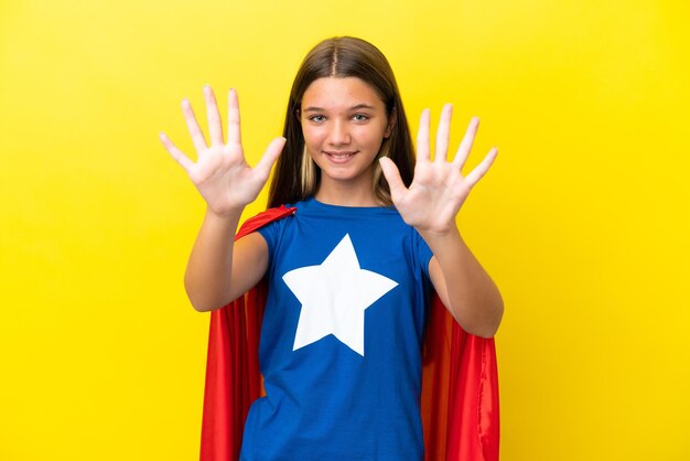 Little caucasian superhero girl isolated on yellow background counting ten with fingers