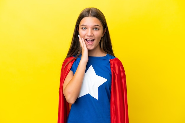 Little caucasian superhero girl isolated on yellow background with surprise and shocked facial expression