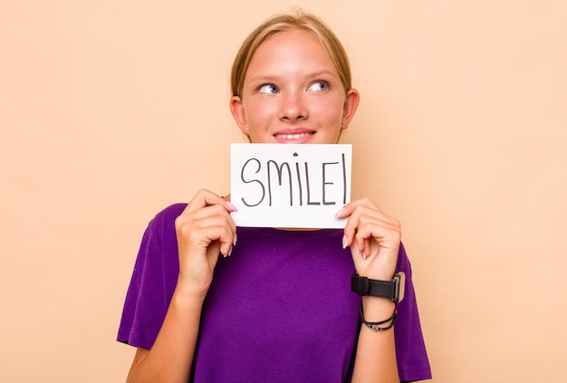 Little caucasian woman holding a smile placard isolated on beige background