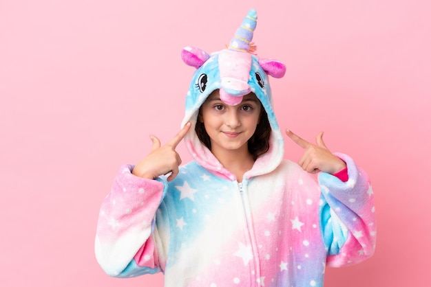 Little caucasian woman wearing a unicorn pajama isolated on pink background giving a thumbs up gesture