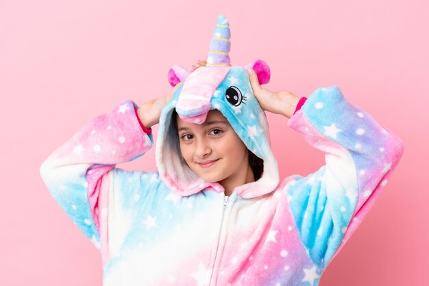 Little caucasian woman wearing a unicorn pajama isolated on pink background