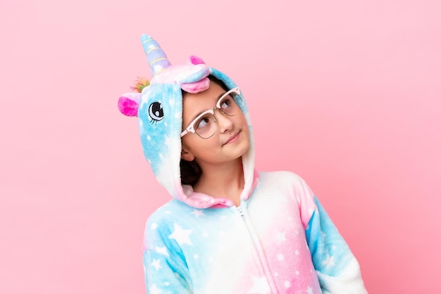 Little caucasian woman wearing a unicorn pajama isolated on pink background