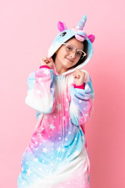 Little caucasian woman wearing a unicorn pajama isolated on pink background