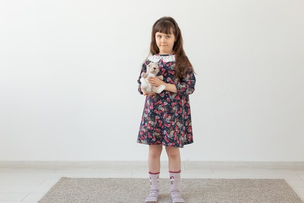 Little charming girl in a flower dress gently embraces her favorite toy bunny standing on a white