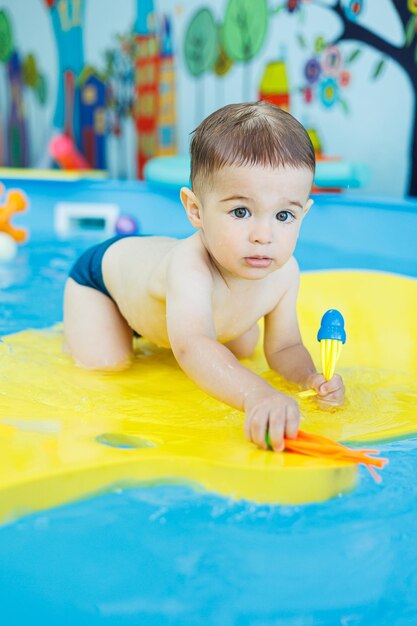 Маленький веселый 2-летний мальчик учится плавать в бассейне Уроки плавания для детей Школа плавания для детей