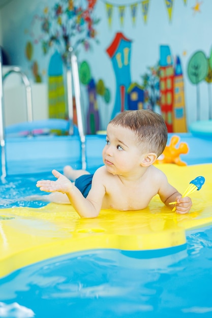 Фото Маленький веселый 2-летний мальчик учится плавать в бассейне уроки плавания для детей школа плавания для детей
