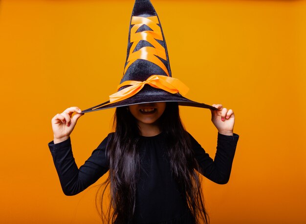 Little cheerful Caucasian girl in Halloween witch costume isolated on yellow background.