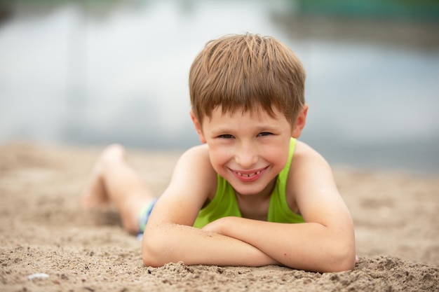 水の近くの砂の中の小さな陽気な子供ビーチで夏服を着た少年の肖像画