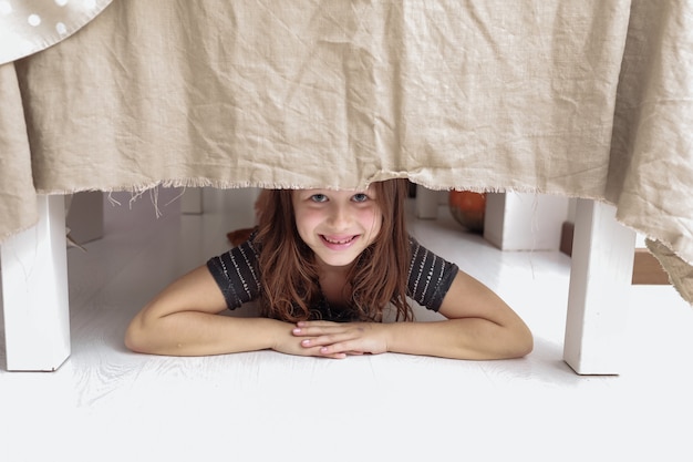 Photo little cheerful girl climbs under the table and grimaces