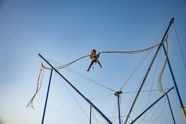 A little cheerful girl flies on springy bright elastic bands and jumps on a trampoline enjoying the long-awaited vacation in the warm sun