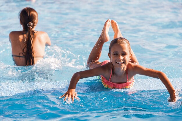 澄んだ澄んだ水とプールで遊んで、カメラに笑みを浮かべて見ている小さな陽気な女の子