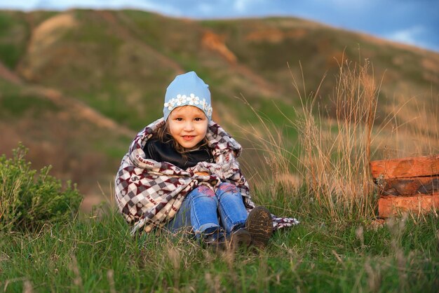 Little cheerful girl preschooler sits on the ground wrapped in a blanket