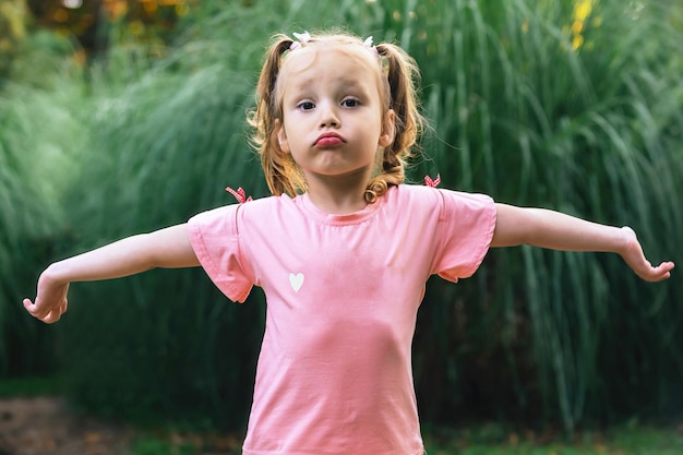 Photo little cheerful girl on a walk in the park spread her arms to the sides gesture don't know