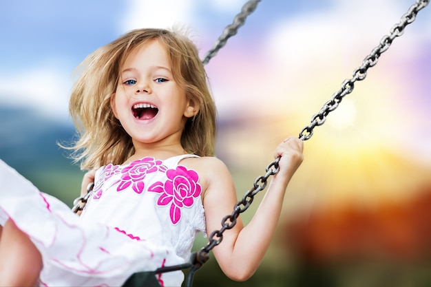 Little child blond girl having fun on a swing