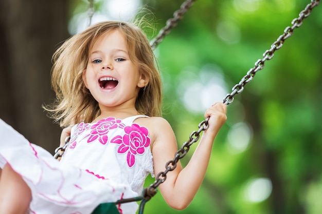 Little child blond girl having fun on a swing