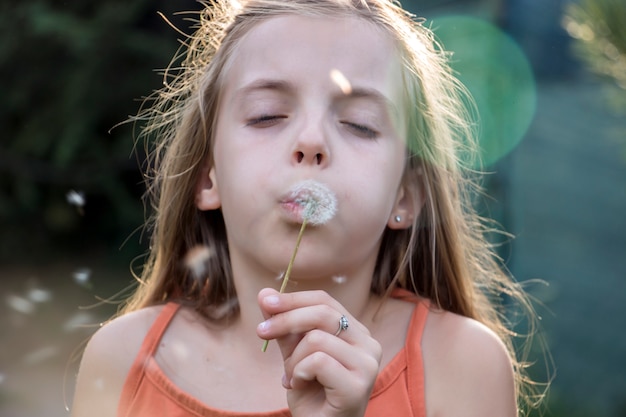 little child blowing dandelion in sunny summer day