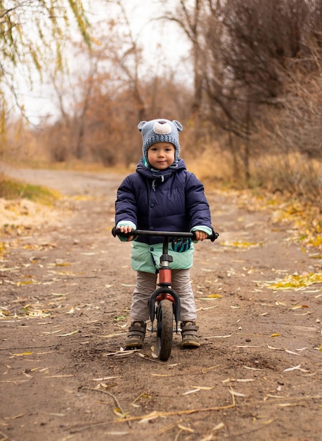 little child in blue clothes looking at camera having fun riding on running bike on road in suburbs