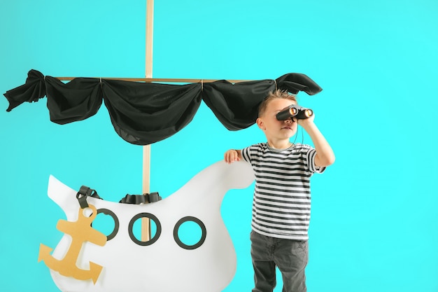 Little child boy playing with cardboard ship on blue wall