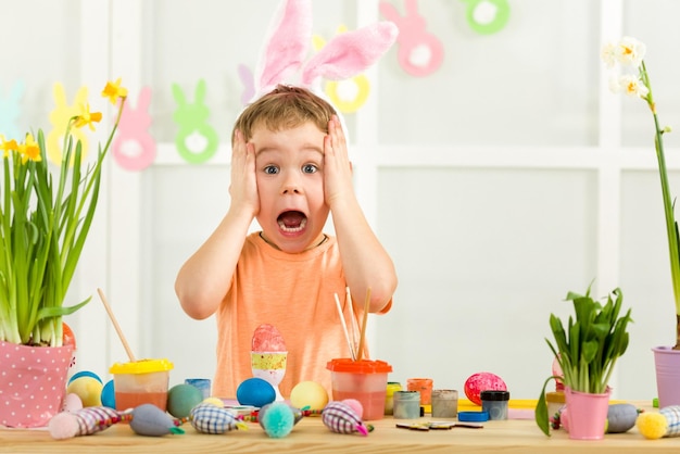 Little child boy with Easter bunny ears painting Easter eggs