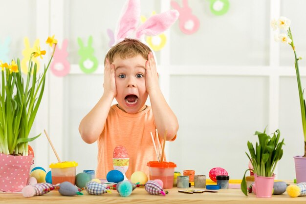 Little child boy with easter bunny ears painting easter eggs