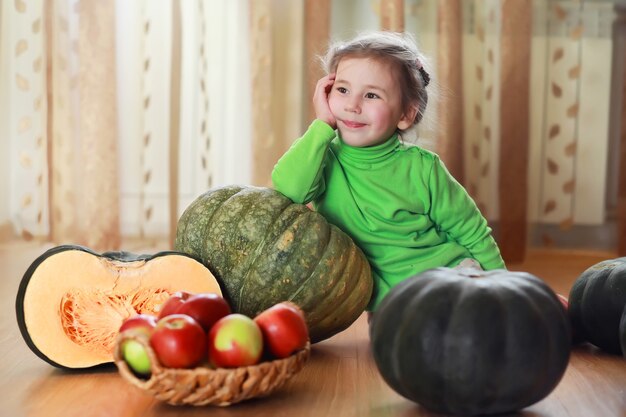 小さな子供は秋にカボチャを選びます。巨大なカボチャに座っている子供。カボチャは、アメリカの祝日であるハロウィーンと感謝祭に使用される伝統的な野菜です。