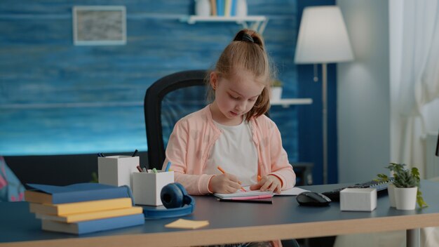 Little child drawing with colorful pencils on notebook at desk