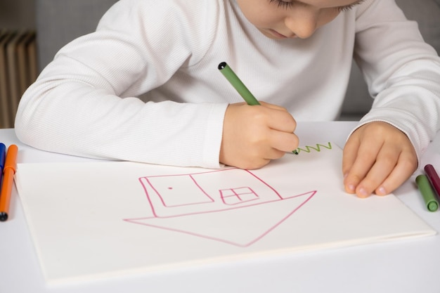Foto piccolo bambino che disegna con penne felttip una casa con l'erba in un quaderno di disegni