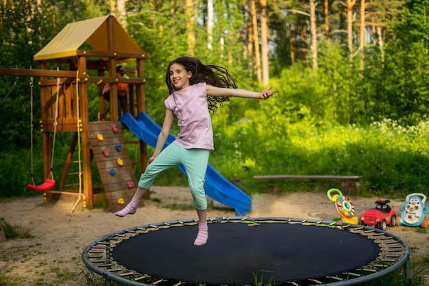 Little child enjoys jumping on trampoline outside in backyard