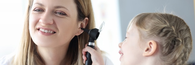 Little child examining doctor ear with otoscope in clinic diagnosis and treatment of ear