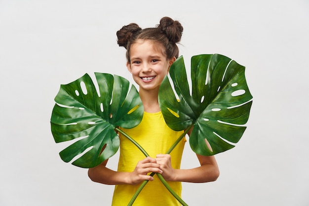 Маленький ребенок девочка 9 лет в желтом платье с большими листьями Монстера в руках.