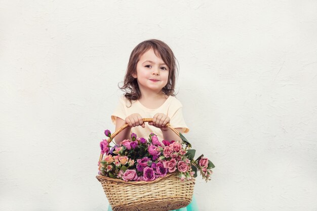 Bambina bella, carina e felice con i fiori sullo sfondo del muro bianco