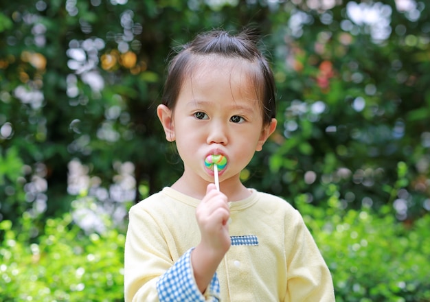 小さな子供の女の子が公園でロリポップキャンディーを食べるのを楽しむ