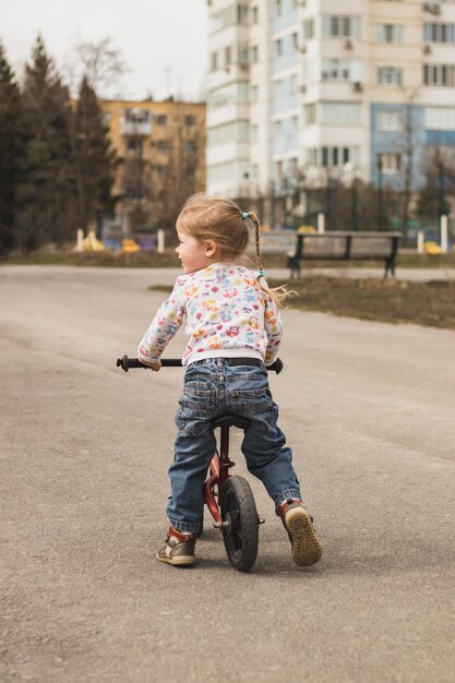 little child girl from behind riding a bike in the city park outdoors