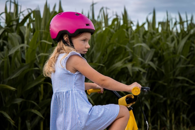 トウモロコシ畑の背景に自転車に乗ってヘルメットをかぶった小さな女の子