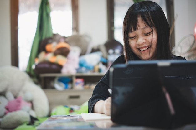 Little child girl looking tablet distance learning class\
watching online lesson with laughing,study in lock down as schools\
closed due to covid-19