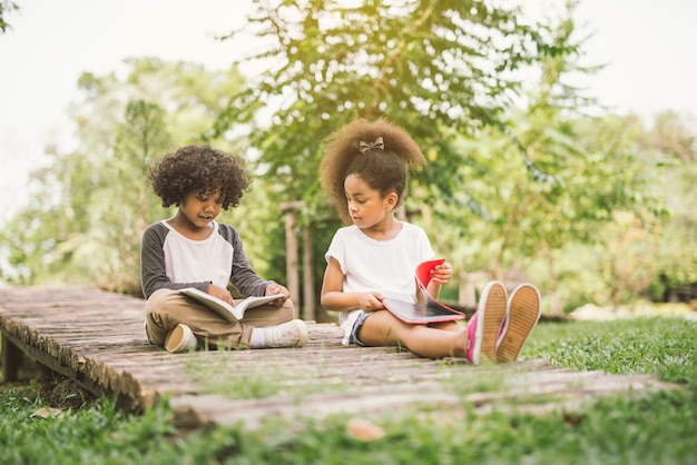 Photo little child girl reading book between green meadow garden with friend education concept