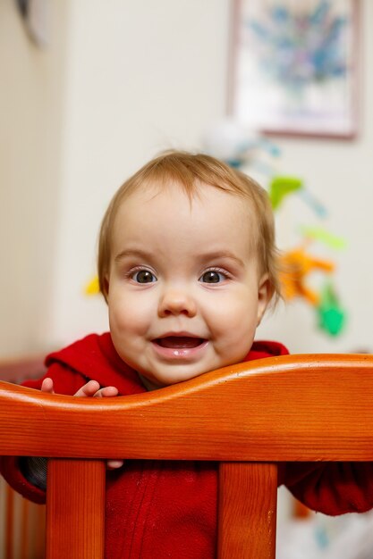 Little child girl in a red sweater, smiles beautifully, in a crib, plays and has fun, emotional photo