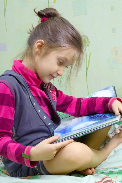 Photo little child girl sitting on a bed and reading a book